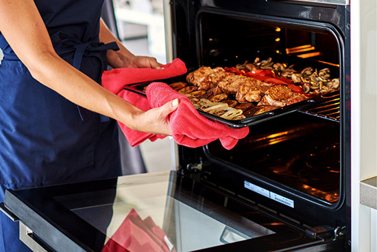 Removing a tray of meat from oven